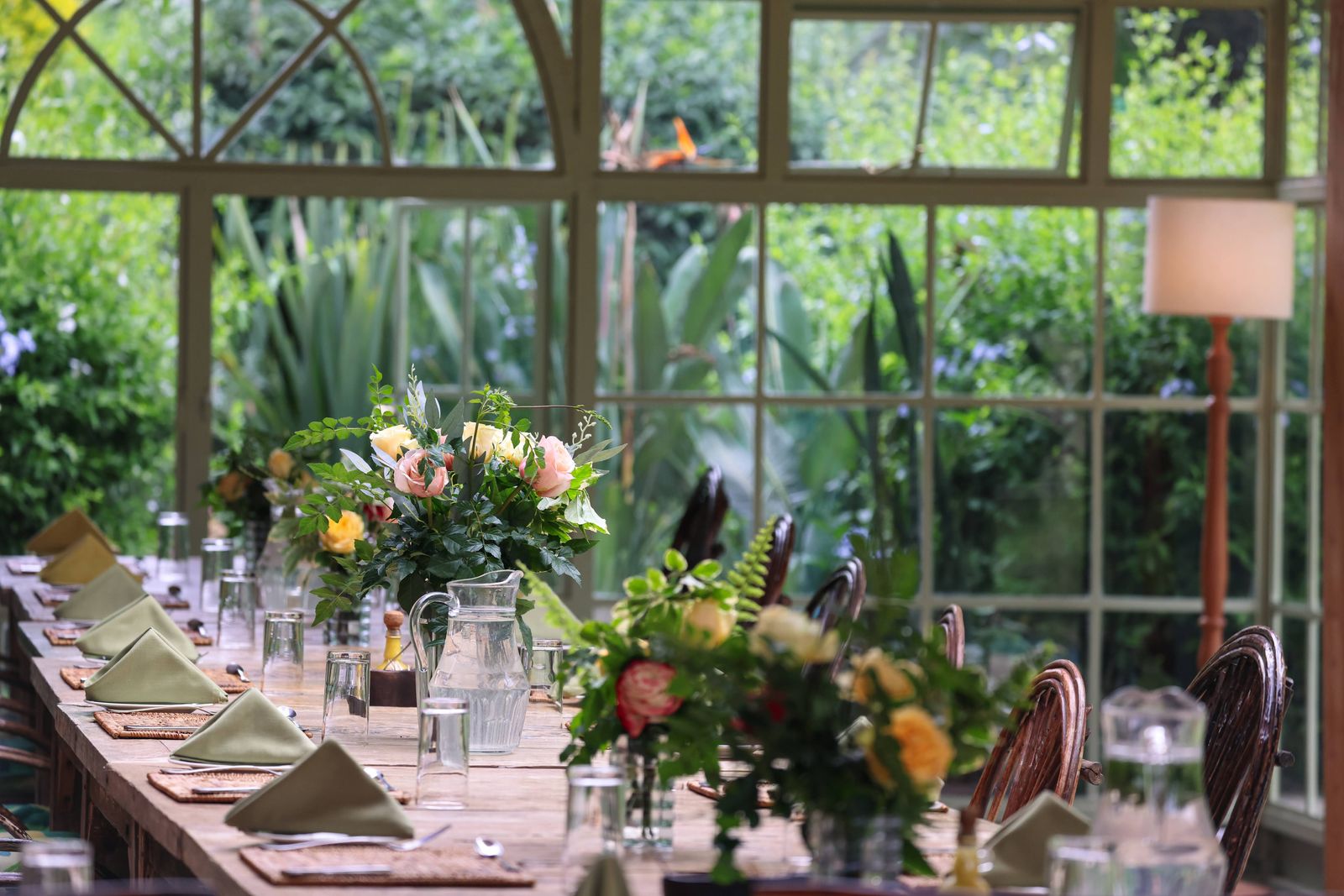 The arched-window conservatory dining room at Mukima Manor, table set with garden roses