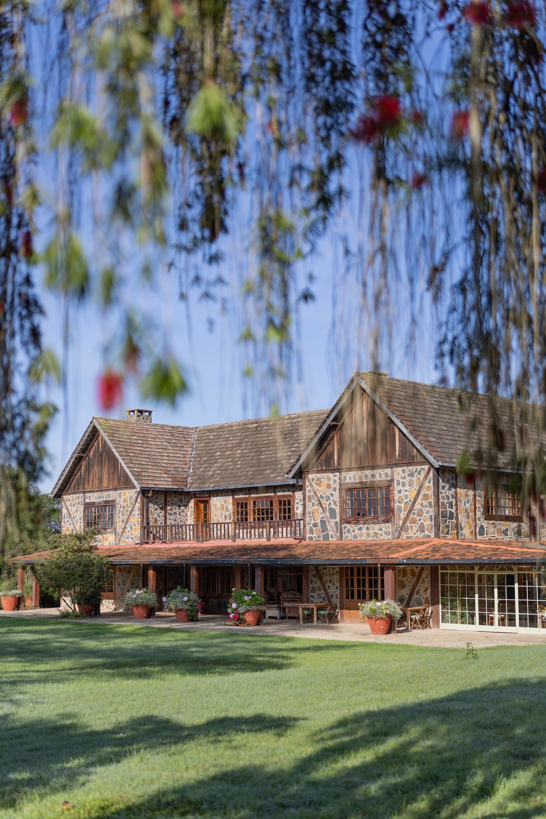 The century-old stone-and-timber manor house at Mukima Manor, willows in the foreground at the foot of Mt Kenya