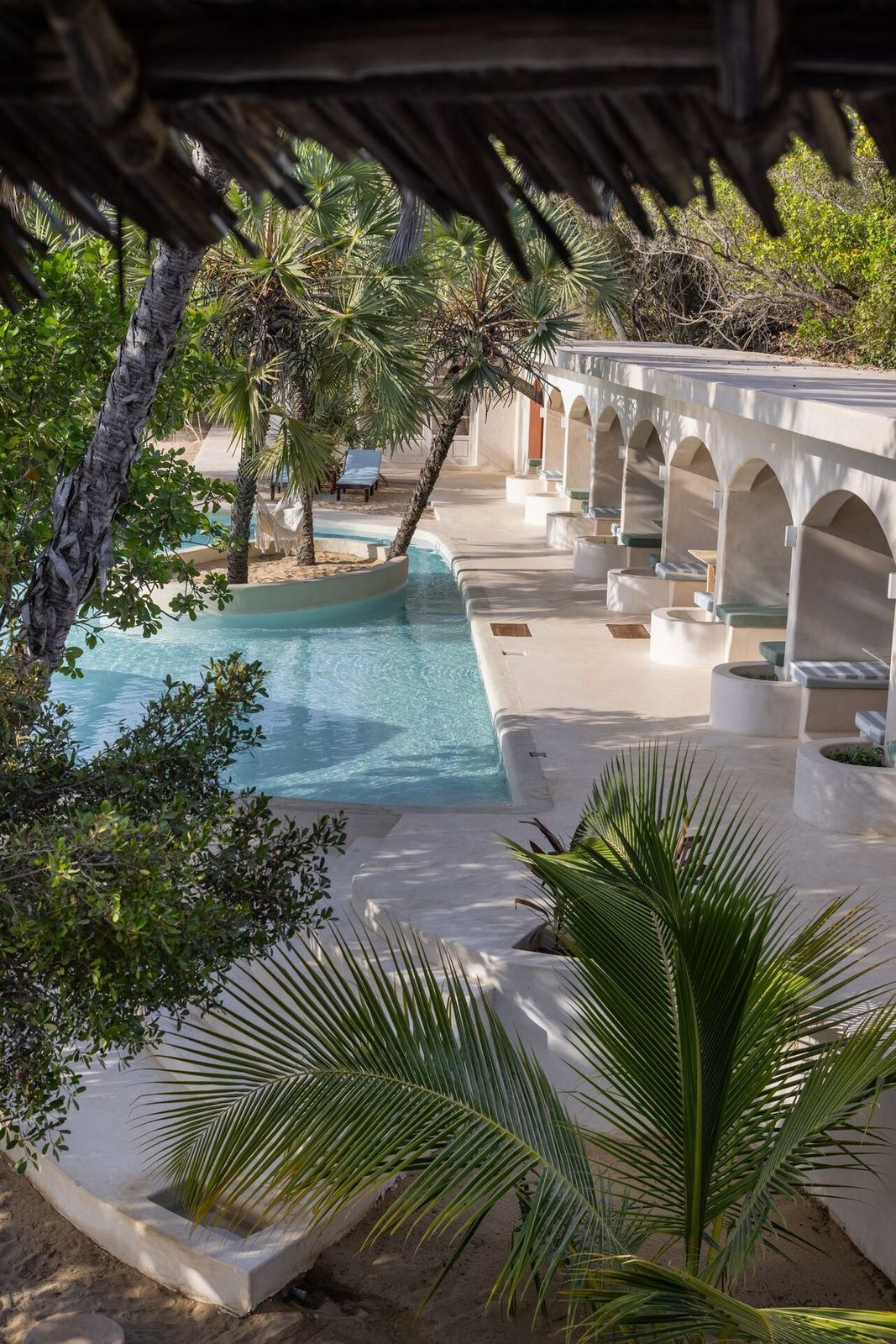 Arched colonnade beside the swimming pool at The Cabanas Lamu, framed by palms and indigenous coastal trees