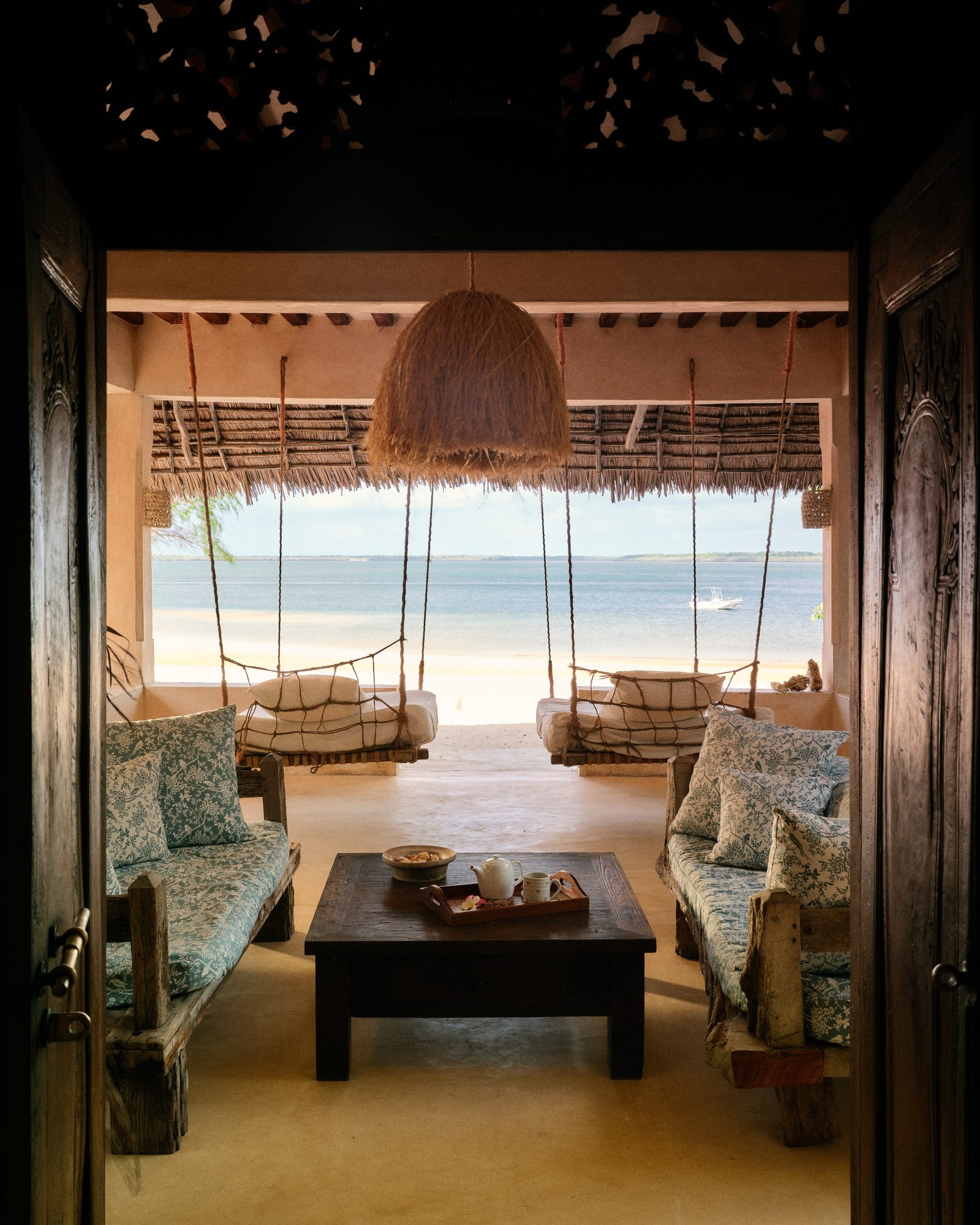 Netted four-poster bed framed by a carved Lamu door at The Cabanas, Kizingoni Beach, Lamu