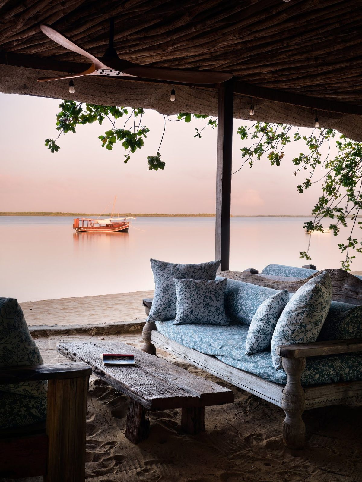 Sandy garden path winding between weathered palm trunks at The Cabanas Lamu, dappled by leaf shadow