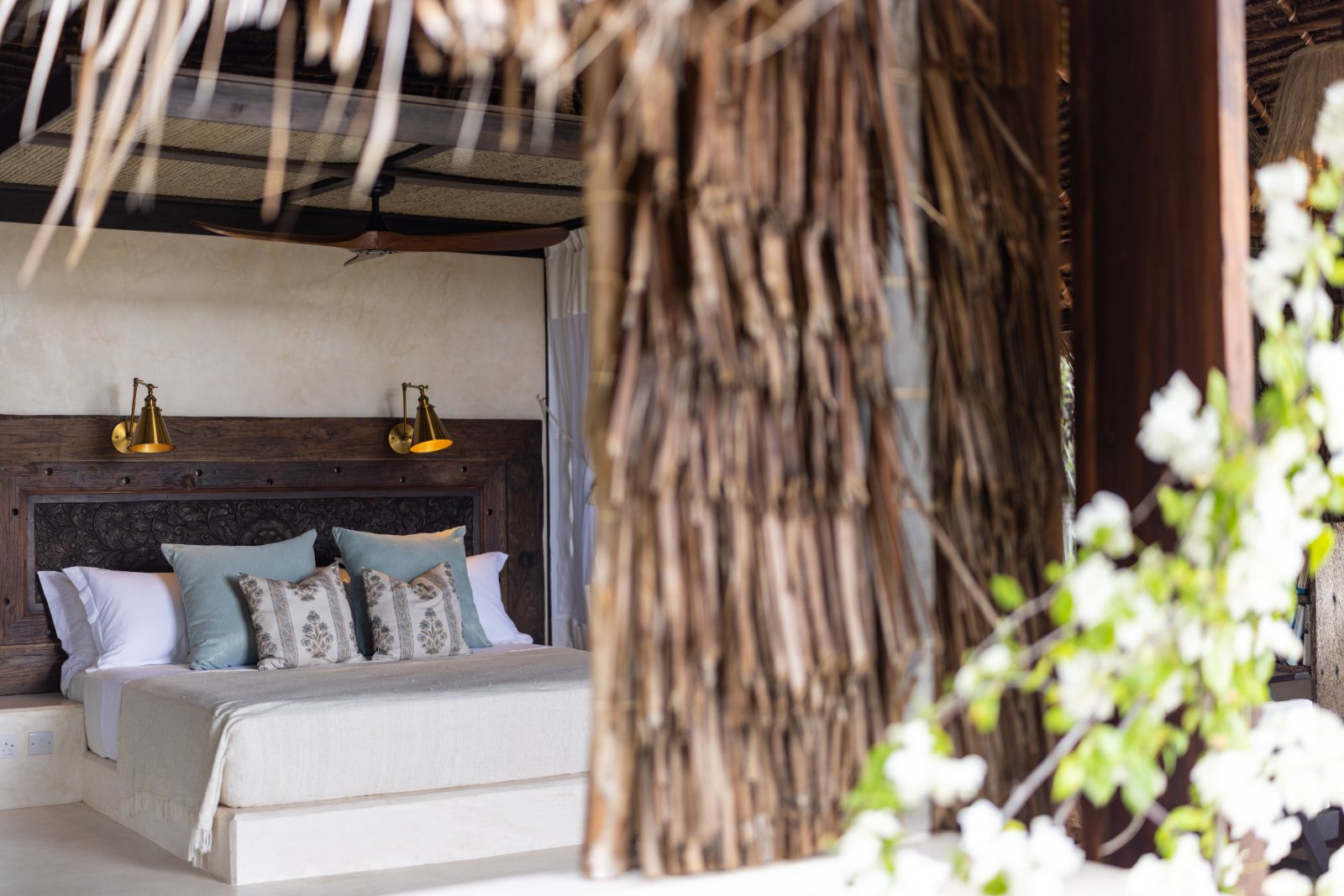 Aloha cabana — bed framed by a makuti thatch column with bougainvillea in flower