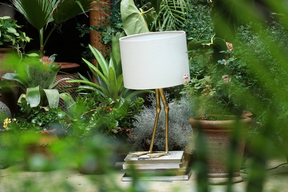 The brass crane-leg lamp from another angle, framed by ferns and Spanish moss