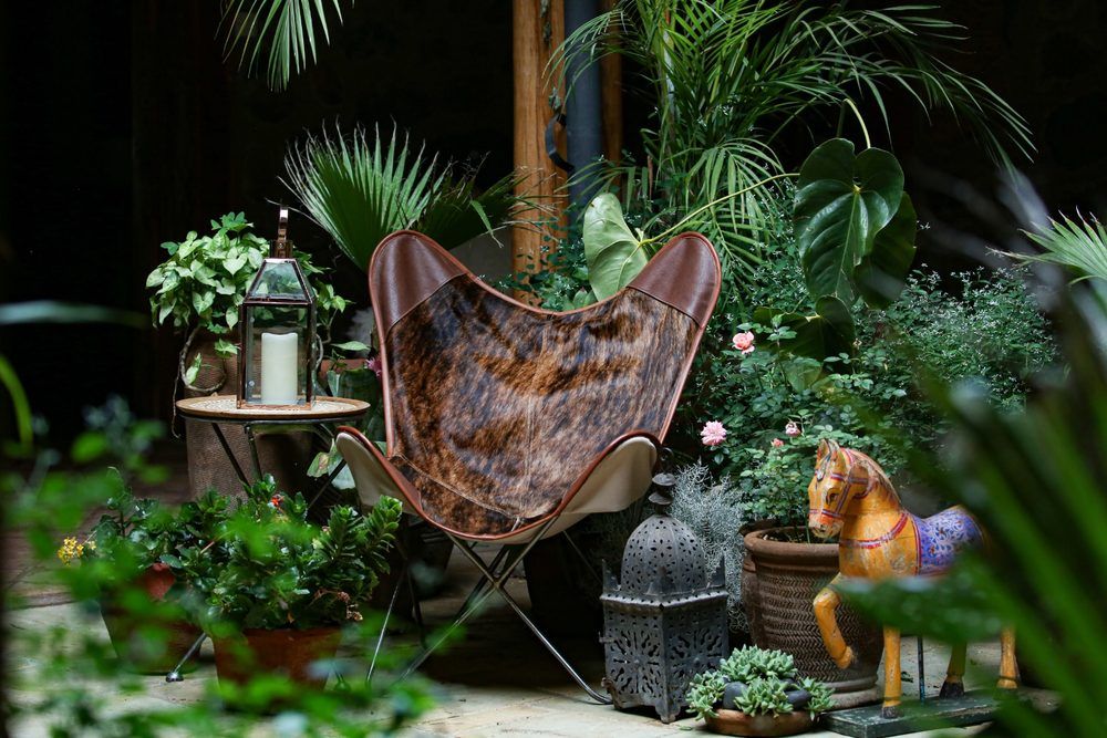 A cowhide butterfly chair in a Lamu courtyard with a brass lantern and a hand-painted carved horse