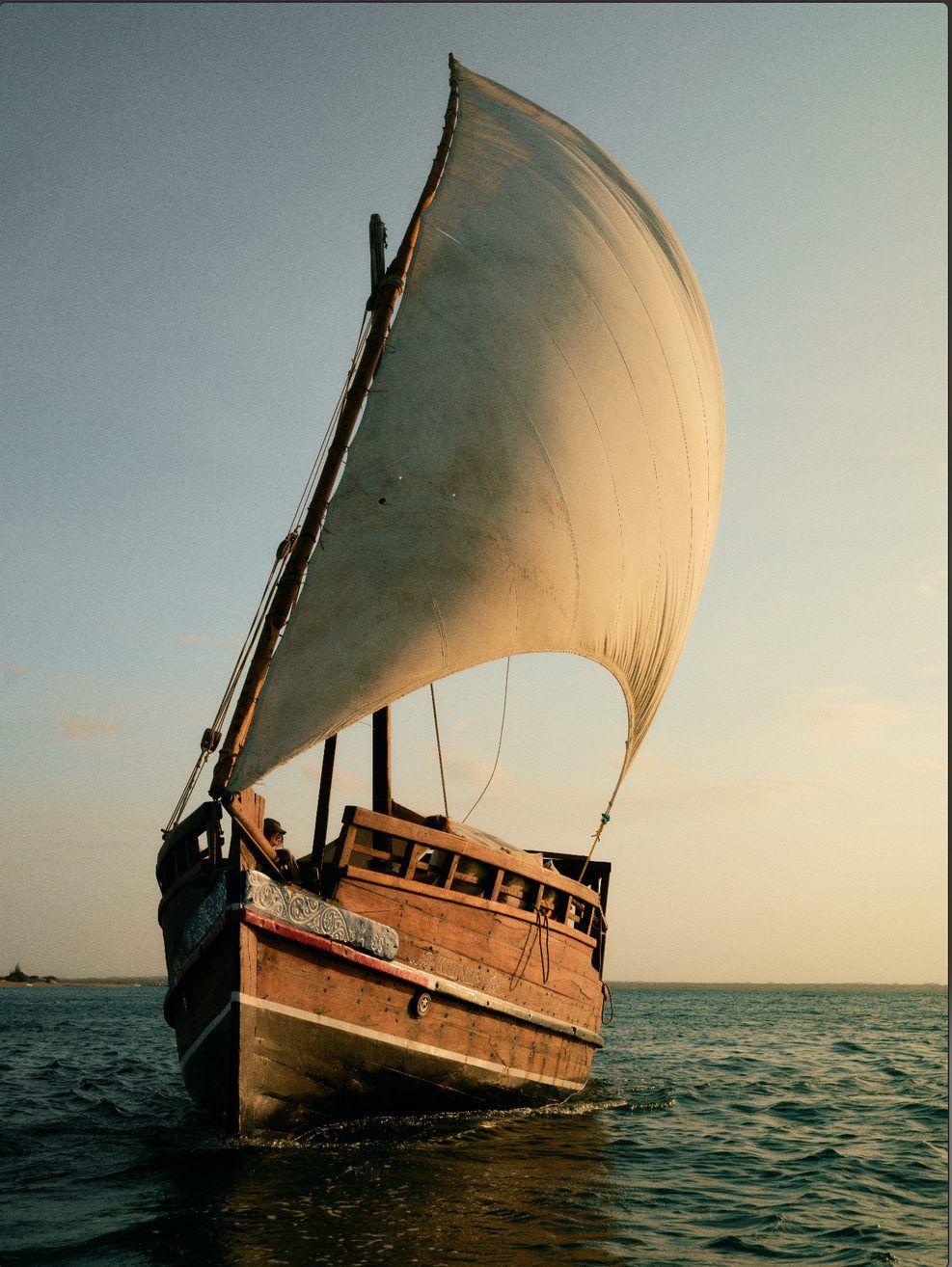 A dhow sailing at sunset on the lagoon, paddleboarders nearby
